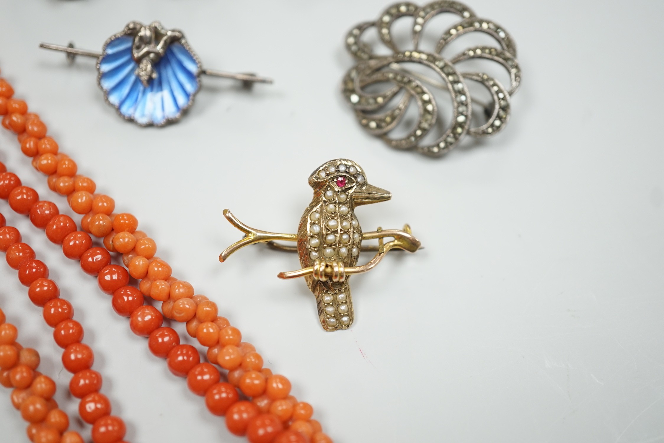 A yellow metal, seed pearl and red stone set 'bird on a branch' brooch, width 30mm, two coral bead necklaces, an enamelled white metal imp and shell brooch, three rings, a marcasite brooch and a simulated pearl necklace.